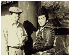 Two Japanese men, one in modern (1950s) clothes, the other in the costume of a man from an ancient Japanese era, pose smiling for the camera