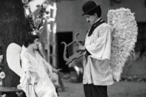 Photo of Charlie Chaplin wearing angel wings (and his trademark bowler hat) talking to a young woman also wearing angel wings