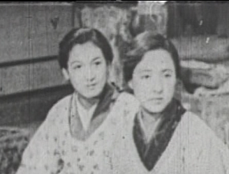 Two modern Japanese women, a young girl and a middle-aged housewife, in traditional dress looking solemnly at someone beyond camera range