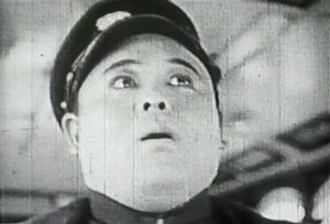 A 20th Century Japanese man in a bus driver's uniform looks up at somthing in a state of shock