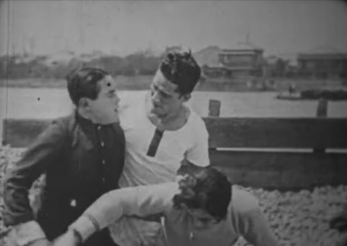 Image of a Japanese man of the 1920s, in modern dress, seizing two smaller men, also in modern dress