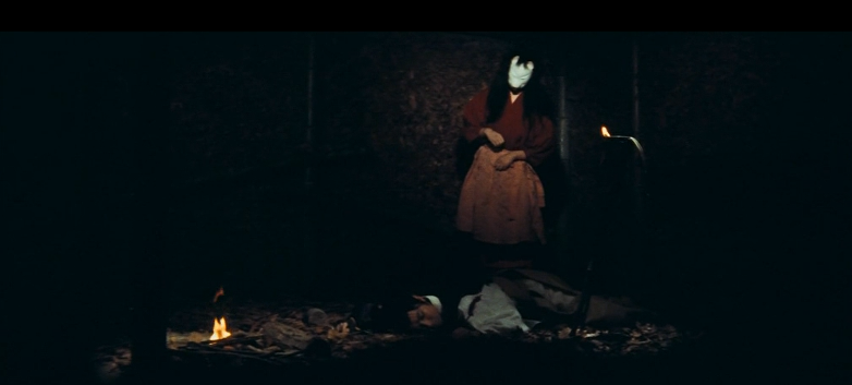 A woman in a fox mask looks down at an unconscious man on the floor of a house at night
