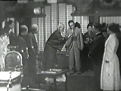 A Japanese man in a suit is attended by a group of about a dozen male and female servants