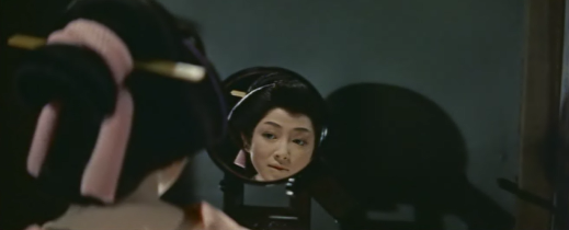 An 18th Century Japanese woman, putting on her makeup, looks at herself in the mirror