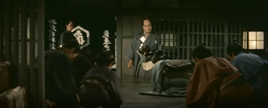 A man from the samurai class confronts the employees of House Kameya while they bow in fear before him