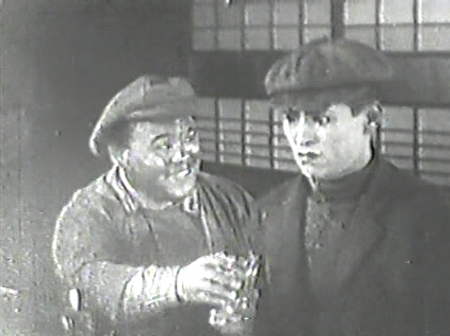 Two Japanese men in working class clothes drink together in a bar
