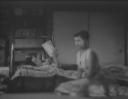 A black-and-white photo of a Japanese man in bed, with a Japanese woman sitting on the floor near him