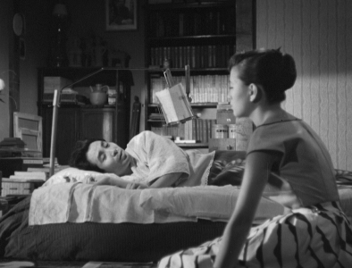 A black-and-white photo of a Japanese man in bed, with a young Japanese woman sitting on the floor near him