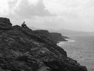 A solitary figure in the far distance sits on an outcropping of rocks, contemplating the sea