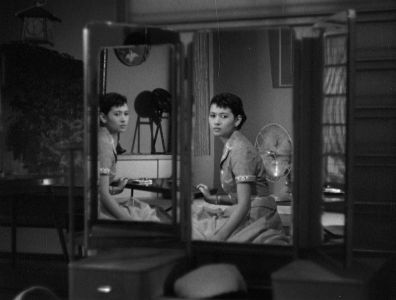 A Japanese woman in modern dress sits in front of facing mirrors, so that two opposing reflections of her can be seen