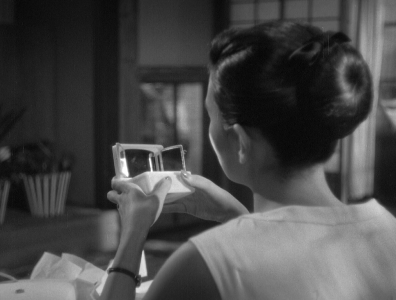 A young Japanese woman in modern clothes, with her back to the camera, gazes at a toy she is holding in her hands showing two miniature facing mirrors