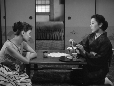 A photo of two Japanese women sitting in an interior space on opposite sides of a table, one wearing modern dress and the other wearing a kimono