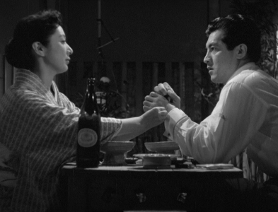 A modern Japanese woman and man face each other across a restaurant table, with the woman putting out a cigarette on the man's hand