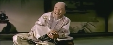 A man in traditional Japanese dress, reclining and laughing