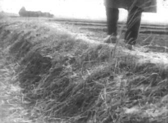 A country road upon which a man, whose feet, legs and coat are alone visible, is walking away from the camera