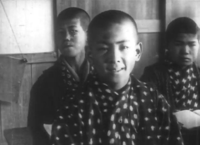 A Japanese boy in a classroom wearing traditional clothes and smiling, with other Japanese boys in the background