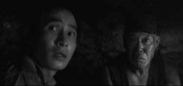 A two-shot of a young man and an older man in a dark mine, looking with fear at something in the distance