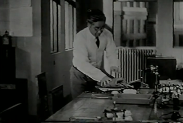 A Japanese man in a business suit in a 1930s-era office folds his suit jacket in the handkerchief he had lain on his desk