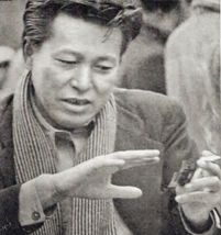 A candid photo of a Japanese man wearing a suit and scarf, gesturing with his hands