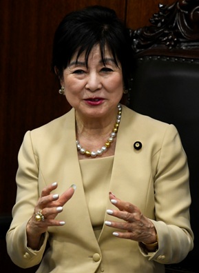 Photo of an elderly, dark-haired Japanese woman in modern dress, gesturing as she is speaking