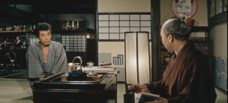 Two seated feudal Japanese men in a room, one young, one middle-aged, face each other in apparent confict