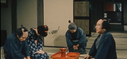 Four Japanese people in feudal clothes sitting in a room: two young people on the left, both weeping, an old woman in the center, also weeping, and a middle-aged man on the right, singing