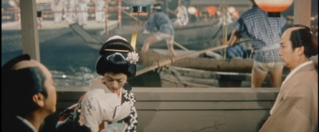 A screenshot from the film in which a feudal Japanese woman in traditional garb, sitting in a boat, looks down in disgust, flanked by two men looking at her with concern