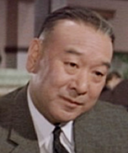 Photo of a middle-aged Japanese man in a business suit, listening to someone just off-camera