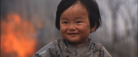 Photo of a smiling Japanese baby in a field, with fire in the background