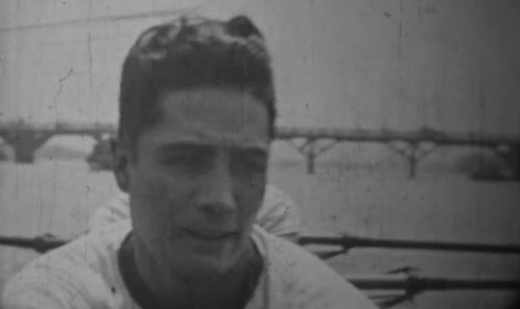 Headshot of a young Japanese man in the 1920's, setting on an unseen boat in the river, with a bridge visible behind him.