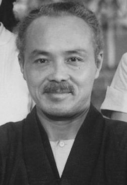A photo of a middle-aged, mustachioed Japanese man, facing the camera and smiling slightly, in traditional dress