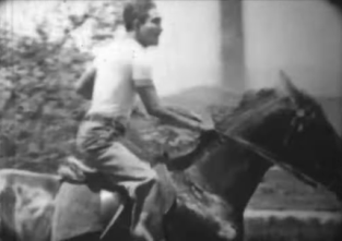 Medium shot of a Japanese man of the 1920s in modern dress riding a horse on a country road
