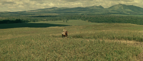 A photo of a vast landscape of mountains and plains with a solitary rider on horseback in the far distance.