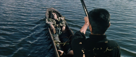A figure in black paddles a canoe on a lake, while another (Japanese) man lies face up near the bow of the ship, seemingly dead