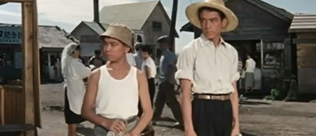 Two young Japanese boys in casual clothing, one a few years older than the other, at an outdoor event are looking at something to their right