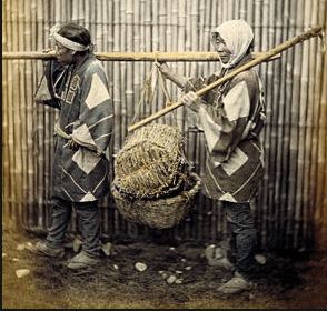 Two 19th Century Japanese, in the clothing of poor peasants, carry a load on a pole between them