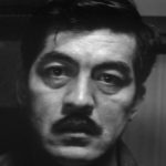 A middle-aged Japanese man with a mustache is looking towards the camera with a distressed expression