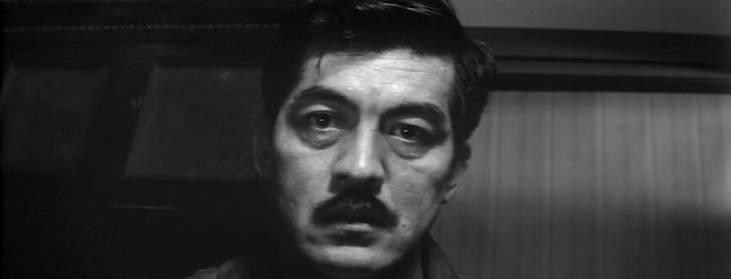 A middle-aged Japanese man with a mustache is looking towards the camera with a distressed expression