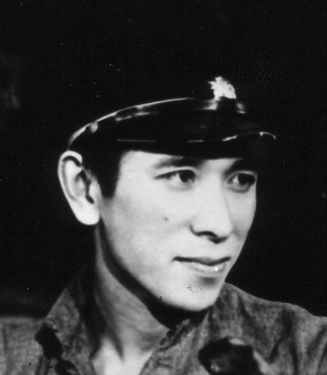 A young Japanese man wearing a cap smiles slightly as he looks to something off to his left