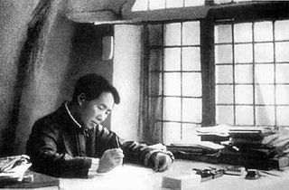 Portrait of young Mao Tse-tung sitting at a desk covered with books and paper, and writing as light pours in through a closed window 
