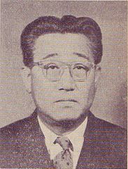 An old headshot photo of a Japanese man in suit and tie wearing glasses