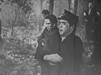 The young Japanese man from the previous photo appears walking in a forest with a number of other young men, all with somber expressions on their faces