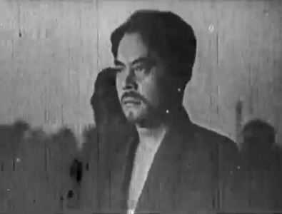 A Japanese man of about 30 with a mustache and wearing traditional clothes walks with a grim, steadfast look towards his destination