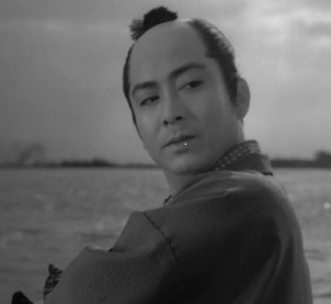 A young man with a samurai topknot and kimono turns his head to look at something offscreen, as a river appears in the background 
