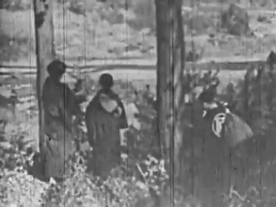 On a hill overlooking a vast field, the young man and his mother, in traditional dress, look out over the scene with their backs to the camera. A boy holding a bag over his shoulder, also back to camera, appears at right