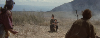 In feudal Japan, a woman and a man in the foreground, both in rough dress, look at a samurai in the background seated on a rock and holding a child in his lap