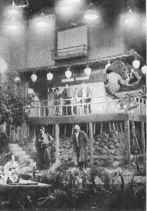 Scene from a movie set depicting a Japanese inn, in which Japanese filmmakers in modern dress (1930s) photograph a group of actors in traditional dress