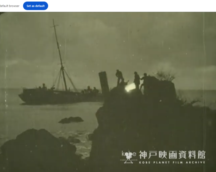 A night scene of a coastline, with a ship, slightly listing, in the background, and a rocky hill in the foreground, on which several people can be seen, silhouetted by a bonfire behind them.
