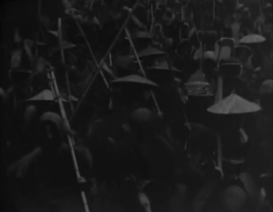 A group of peasant women wearing sedge hats and carrying farming tools, all facing the camera, march together in the pre-dawn darkness