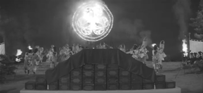 A stage showing a troupe of female Japanese dancers is seen in the middle distance, their performance illuminated by torches and by a firework depicting a symbol of the shōgun